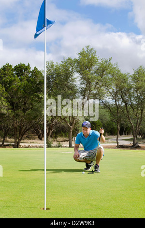 Giovane uomo accovacciata alla figura fuori il meglio possibile colpo a un campo da golf Foto Stock