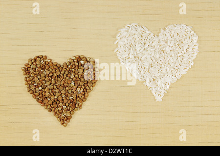 Riso e grano saraceno a forma di cuore sul pannello di legno Foto Stock