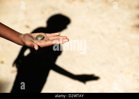 Povero indiano childs mano tesa a mendicare tenendo Rupia delle monete in euro e di ombra. India. Messa a fuoco selettiva con spazio di copia Foto Stock