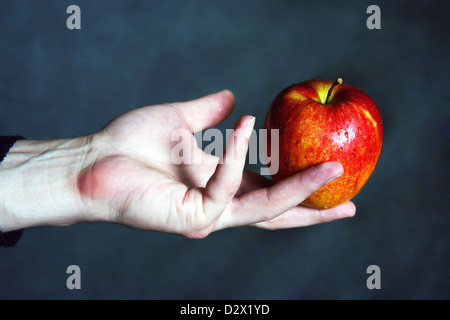 Mano d'uomo con una mela rossa su uno sfondo scuro Foto Stock