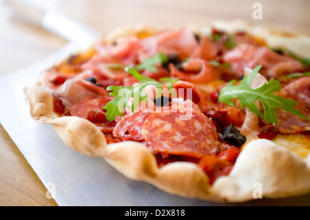 Pizza Anti Pasti, Margherita drappeggiati con salumi roquito, peperoni, olive e vestito razzo. Accompagnare con un bicchiere di vino. Foto Stock