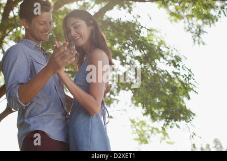 Coppia sorridente tenendo le mani sotto agli alberi Foto Stock