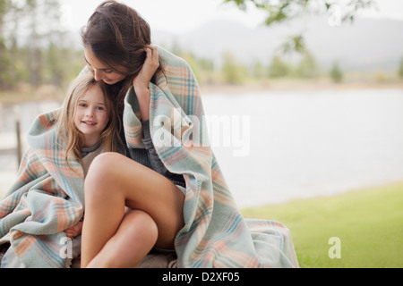 Ritratto della figlia sorridente avvolto in una coperta con la madre a Lakeside Foto Stock