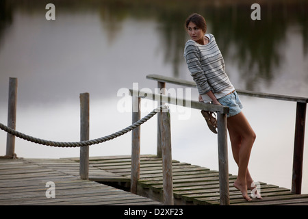 Donna appoggiata sulla ringhiera sul dock sul lago Foto Stock