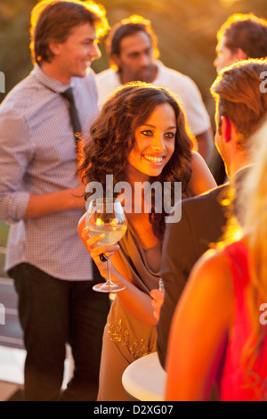 Donna sorridente con bicchiere di vino a parlare con l'uomo sul balcone soleggiato Foto Stock