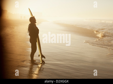 Surfer in piedi con la scheda sulla spiaggia Foto Stock