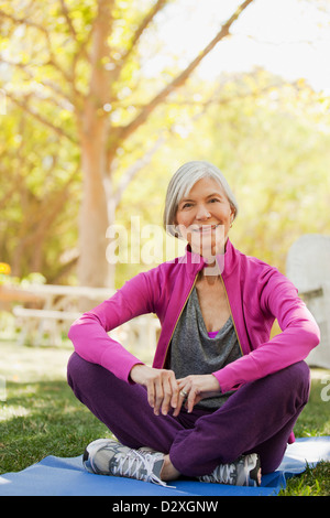 Donna anziana seduta sul tappeto di yoga all'aperto Foto Stock