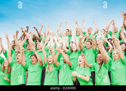 La folla in t-shirt verdi il tifo con le braccia sollevate Foto Stock