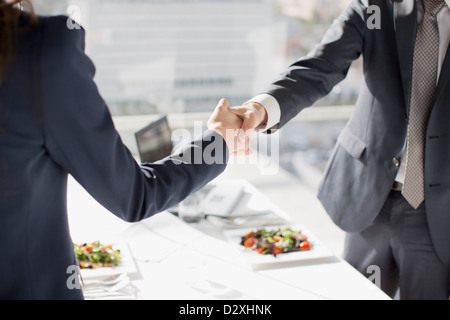 Imprenditore e imprenditrice stringono le mani a tavola con pranzo Foto Stock