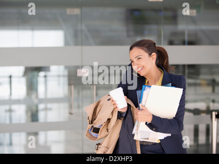 Sorridente imprenditrice il multitasking sul telefono cellulare con caffè e dei documenti Foto Stock
