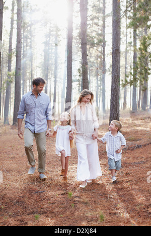 La famiglia felice tenendo le mani e camminare nei boschi di sole Foto Stock