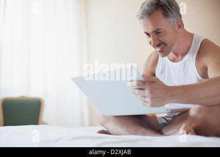 Uomo sorridente con notebook a letto Foto Stock