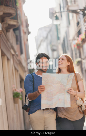 Coppia sorridente camminando con la mappa su strada stretta a Venezia Foto Stock