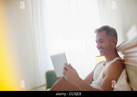 Uomo sorridente con tavoletta digitale a letto Foto Stock