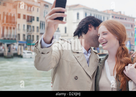 Ridendo giovane tenendo autoritratto con la fotocamera del telefono a waterfront di Venezia Foto Stock