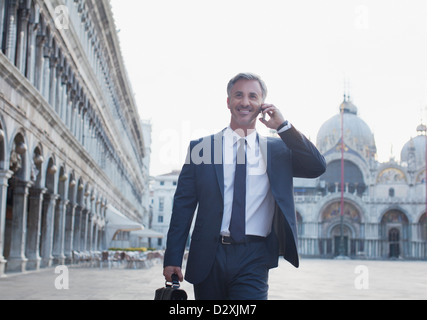 Imprenditore sorridente parlando al cellulare e a piedi attraverso Piazza San Marco a Venezia Foto Stock