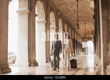 Imprenditore sorridente e imprenditrice tirando le valigie lungo il corridoio a Venezia Foto Stock