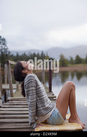 Donna sorridente seduto sul dock a Lakeside con testa indietro Foto Stock