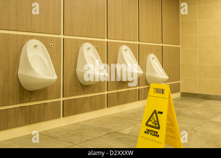 Fila di orinatoi e pavimento bagnato segno in bagni Foto Stock