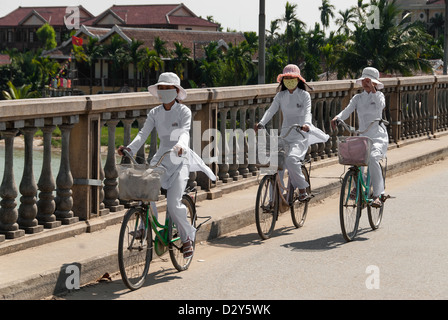 Tre ragazze non identificato in abiti tradizionali cavalcare le loro biciclette su un ponte su Gennaio 8, 2008 a Hoi An, Vietnam. Foto Stock
