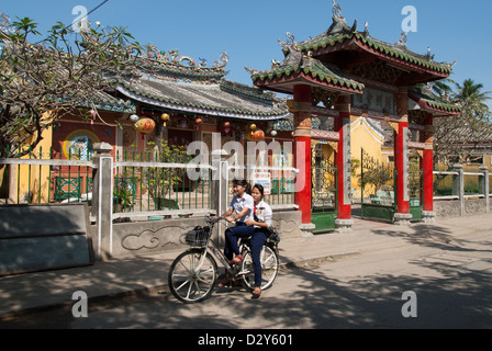 Due ragazze non identificato guidare la propria bicicletta davanti a un tempio buddhistic su Gennaio 8, 2008 a Hoi An, Vietnam. Foto Stock