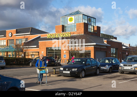 Donna spingendo carrello della spesa in parcheggio, Morrisons supermercato Tredegar, Blaenau Gwent, Wales, Regno Unito Foto Stock