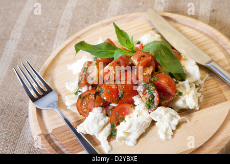 Insalata Caprese su un round scorza di legno con coltello e forchetta Foto Stock