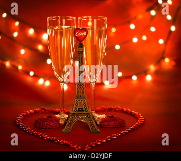 Foto di due parti in vetro con champagne decorata con piccola torre Eiffel e a forma di cuore le candele e i talloni su sfondo rosso Foto Stock