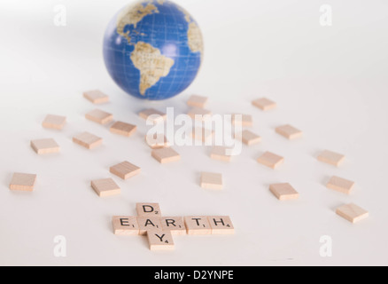 Concetto: "La Giornata della Terra' enunciato nelle lettere di Scrabble con fuori fuoco globo in background. Isolato su sfondo bianco. Foto Stock