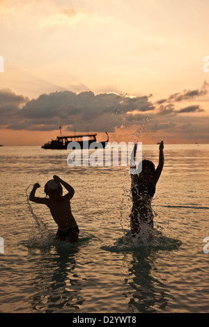 I bambini gli schizzi a bordo delle acque, tramonto su Kuda Hura, Maldive Foto Stock