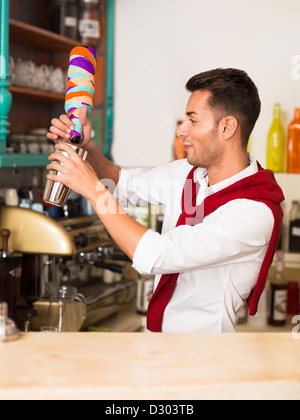 Giovani caucasici attraente barista versando bevande da un vaso colorato avvolto in carta in uno scuotitore Foto Stock