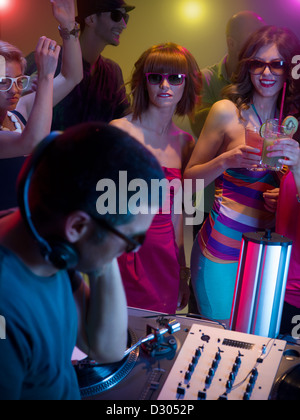 Dj di musica di miscelazione con il giradischi a parte con attraenti giovani ragazze felici ballare davanti a lui con gli occhiali da sole e cocktail Foto Stock