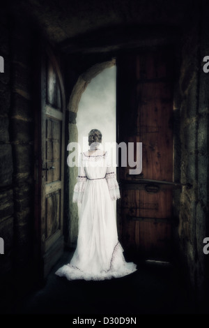 Una donna in un elegante abito è in piedi al gate di un vecchio castello Foto Stock