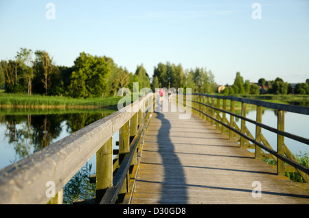 Lunga passerella in legno con ringhiere sopra il lago e sfocata la gente a piedi di distanza. Foto Stock