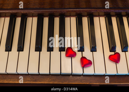 Cuore rosso forme resto sui tasti di un vecchio pianoforte verticale. Foto Stock