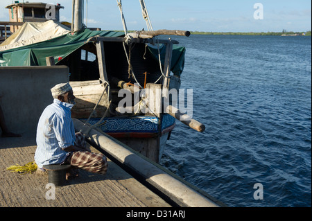 Uomo seduto sul pontile di Lamu town, l'arcipelago di Lamu, Kenya Foto Stock