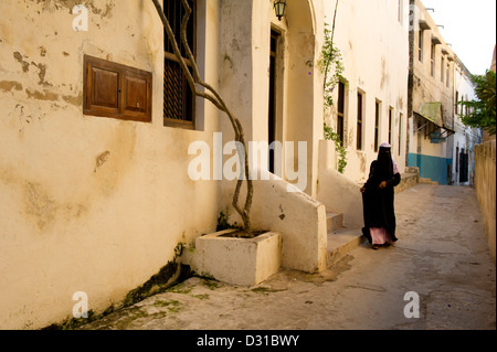 Donna musulmana a piedi attraverso un vicolo di Lamu town, l'arcipelago di Lamu, Kenya Foto Stock