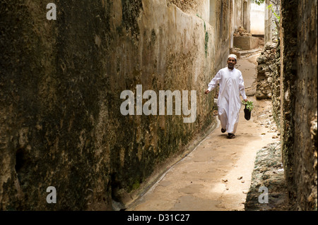 Uomo che cammina attraverso uno stretto vicolo della città di Lamu, l'arcipelago di Lamu, Kenya Foto Stock