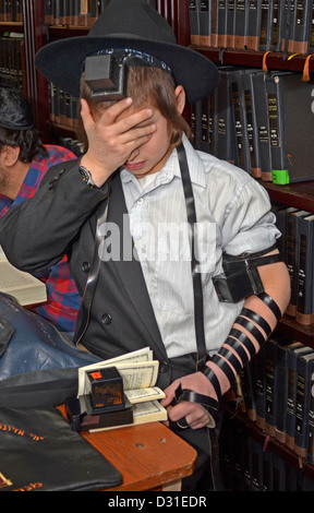 Dodici anni e dieci mesi vecchio ragazzo che prega con i filatteri (tefillin) per la prima volta. A Lubavitch sede a Brooklyn. Foto Stock