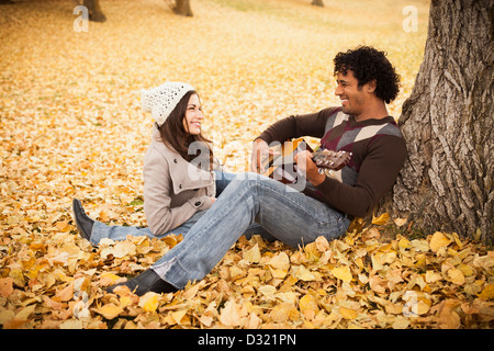 Uomo a suonare la chitarra per ragazza in foglie di autunno Foto Stock