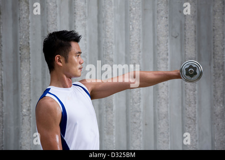 Atletica Giovane uomo cinese esercizio con manubri. Muscoloso uomo asiatico che esercitano con peso di apparecchiature per il training. Foto Stock