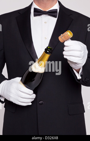 Cameriere di apertura di una bottiglia di champagne tenendo il tappo di sughero nella sua altra mano. Foto Stock