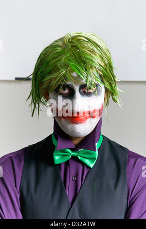 Young man dressed up like The Joker with crazy green hair very messy makeup wearing small green bow tie, purple collard shirt Foto Stock