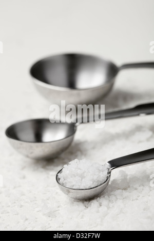 Riduzione di assunzione di sale. Diverse dimensioni di cibo misurini dove il più piccolo cucchiaio è riempito con sale marino. Foto Stock