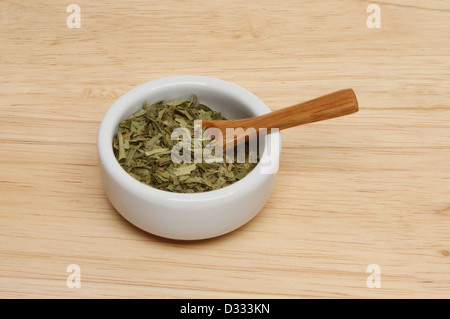 Essiccato di dragoncello foglie di erbe in un ramekin con un cucchiaio di legno su una tavola di legno Foto Stock