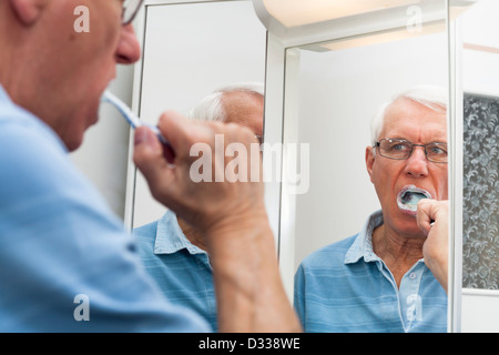 Close up di senior uomo riflette in specchio spazzolando i suoi denti. Foto Stock