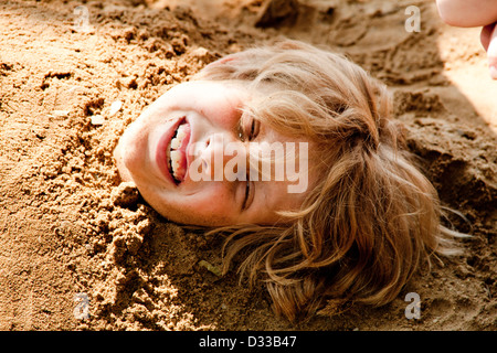 Ragazzo sepolto nella sabbia fino al collo con Medusa-come capelli biondi. Foto Stock