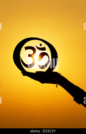 Mano azienda OM indù / simbolo AUM al tramonto. India. Silhouette Foto Stock