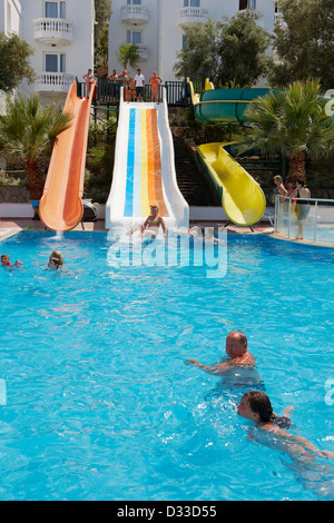 I turisti nuotano in una piscina con scivoli d'acqua al Caliente Bodrum Resort Hotel. Villaggio di Torba, Penisola di Bodrum, Turchia. Foto Stock