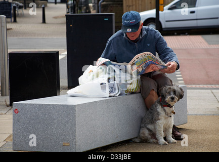 Un uomo seduto sul posto con borse della spesa leggendo il giornale del Sunday Times con il cane seduto ad aspettare pazientemente Cowes Isola di Wight, Hampshire, Regno Unito Foto Stock